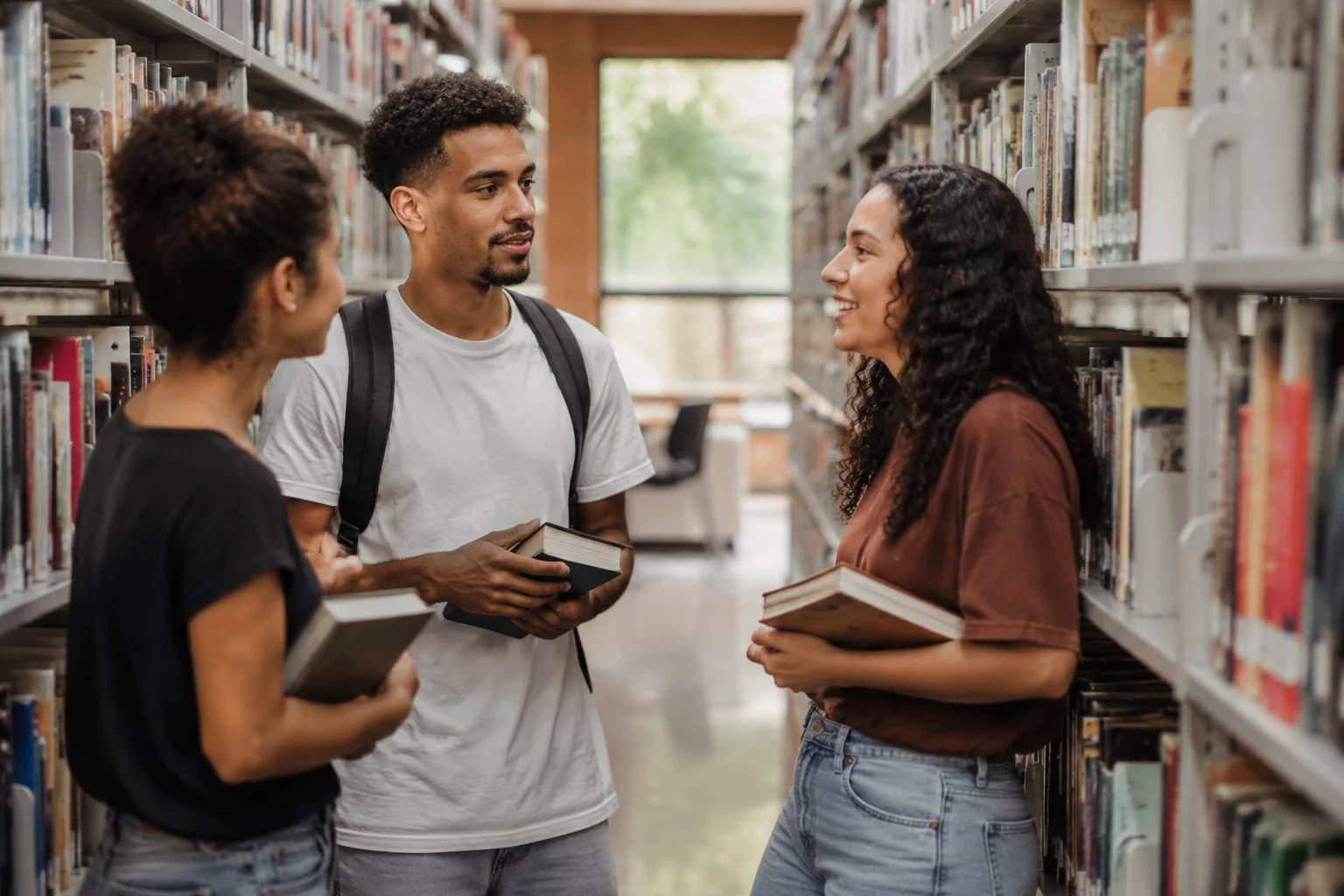 Estudantes conversando em pé entre as estantes de uma biblioteca